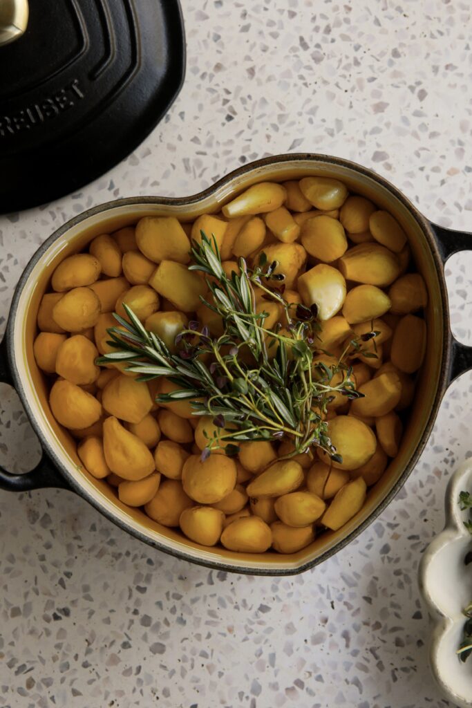 Garlic confit in a small pot, topped with rosemary and thyme after baking.