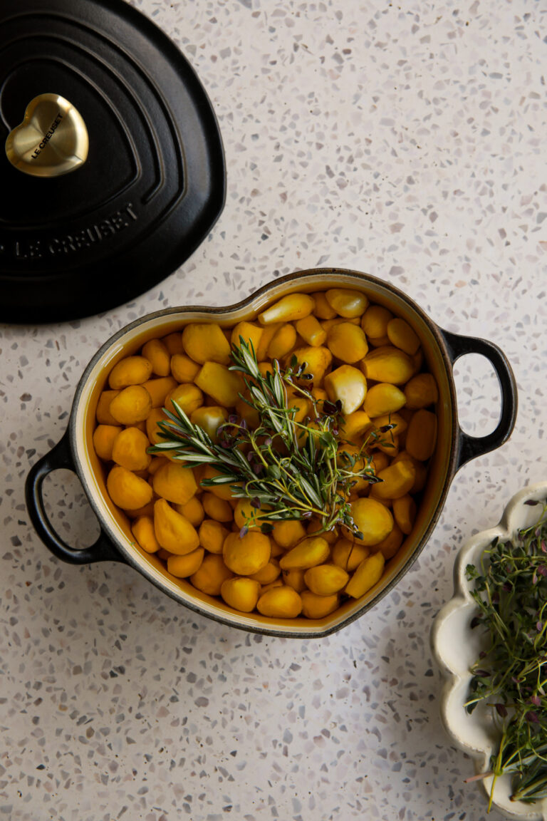 Garlic confit in a small pot, topped with rosemary and thyme after baking.