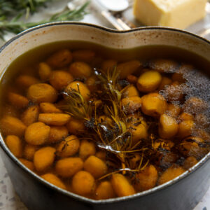 Garlic confit recipe cooking in a heart-shaped pot filled with olive oil, herbs, and caramelized cloves.