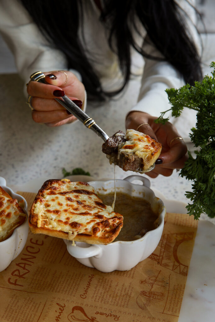 Spoon lifting a bite of cheesy French Onion Cheesesteak Soup with caramelized onions and steak philly cheesesteak soup
