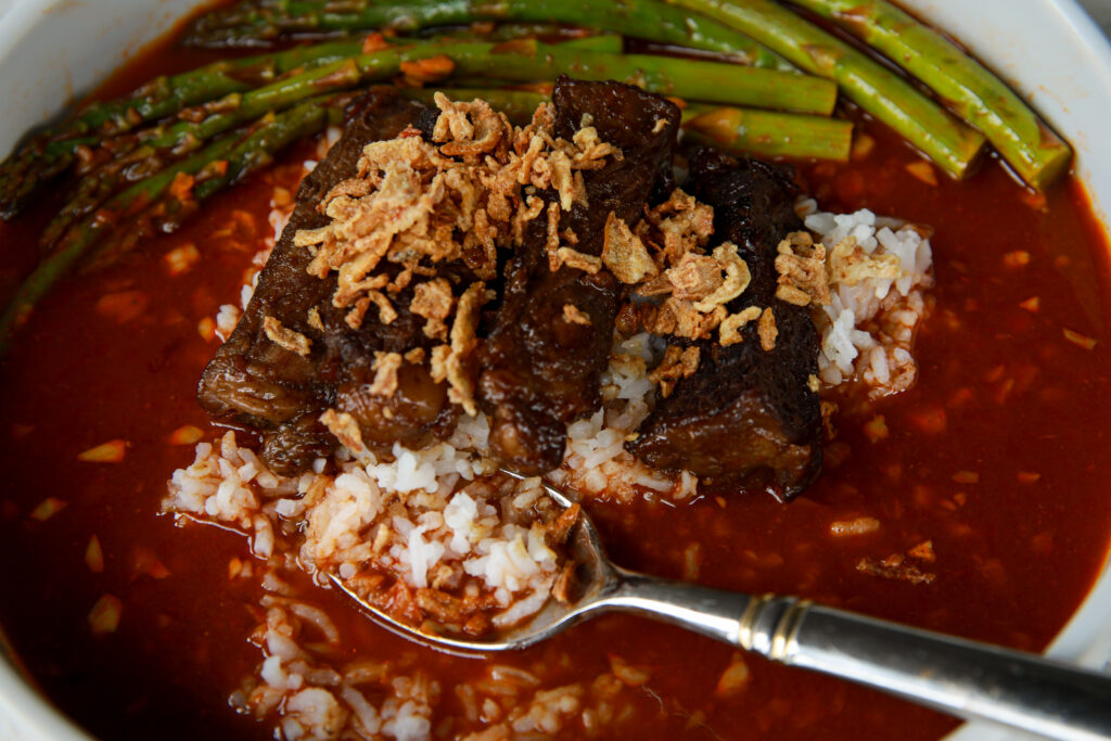 Sticky steak rice bowls served with spicy tomato gochujang broth, fluffy rice, asparagus, and crispy onions in a cozy overhead shot.