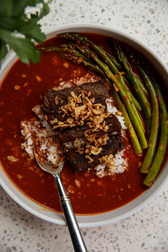 Close-up of sticky steak rice bowls with tender steak, fluffy rice, spicy tomato gochujang broth, and crispy onions.